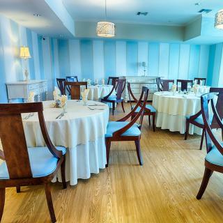 An elegant dining room with round tables set for guests, featuring blue walls and wooden floors.