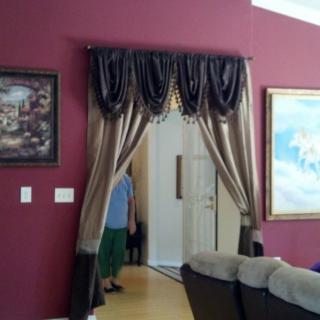 A living room with burgundy walls, adorned with elegant curtains and framed artwork.