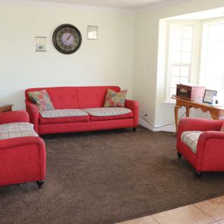A cozy living room with red sofas and a matching armchair, complemented by a dark carpet and a wall clock.