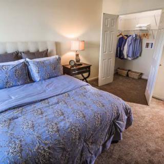 A cozy bedroom with a neatly made bed and an open closet.