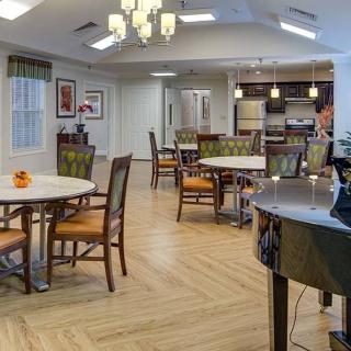 A modern dining area with wooden tables and chairs, featuring an open kitchen and elegant lighting.