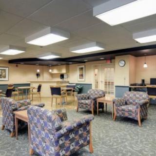 A spacious waiting room with patterned chairs and tables, featuring bright overhead lighting.