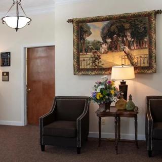 A cozy waiting room with two chairs, a decorative lamp on a table, and artwork on the wall.