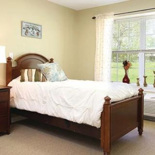 A cozy bedroom featuring a wooden bed, a side table with a lamp, and a large window with sheer curtains.
