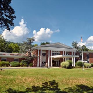 A modern building with a welcoming entrance, surrounded by lush greenery and a clear blue sky.