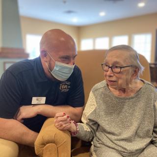 A healthcare worker in a mask conversing with an elderly person in a nursing home.