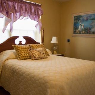 A cozy bedroom with a neatly made bed and decorative pillows, featuring a window with curtains and a bedside lamp.