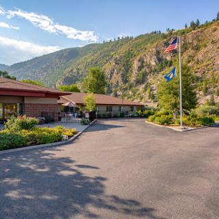 A picturesque view of a building set against a mountainous backdrop, featuring flags and lush greenery.