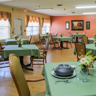 A cozy dining area with green-clothed tables and flower arrangements, perfect for communal meals.