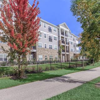 A modern apartment building surrounded by trees with autumn foliage and a sidewalk in the foreground.