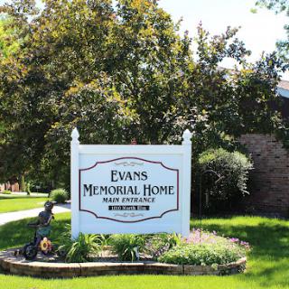 A view of the Evans Memorial Home sign set in a well-maintained outdoor landscape.