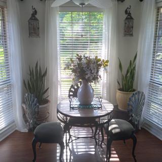 A cozy dining nook with a round table, surrounded by chairs and decorated with plants, basking in natural sunlight.