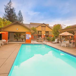 A serene outdoor swimming pool area with surrounding patio furniture and a building in the background, set against a clear sky.