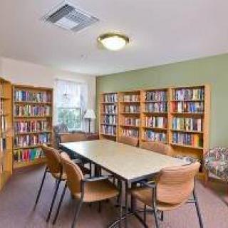 A cozy library reading room with bookshelves and a central table surrounded by chairs.