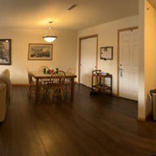 A cozy dining room with a wooden table and chairs, featuring warm lighting and a polished wooden floor.
