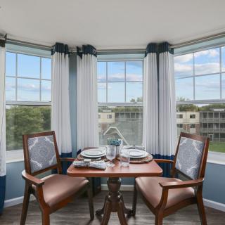 A cozy dining area with a small table set for two, surrounded by large windows allowing natural light to fill the space.