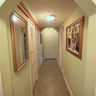 A narrow hallway with a mirror and paintings on the walls, featuring a tiled floor and overhead lighting.