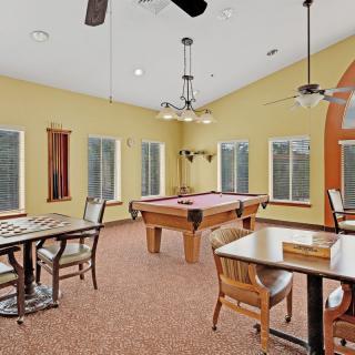 A spacious game room featuring a pool table, chess table, and ample seating with large windows.