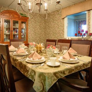 An elegantly set dining room table with a chandelier overhead and a china cabinet in the corner.