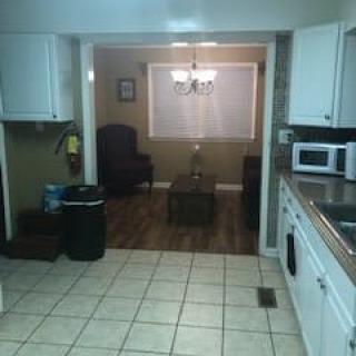 View of a kitchen leading into a living room area with white cabinets and tiled flooring.
