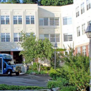A view of a building with a bus parked nearby, surrounded by greenery.