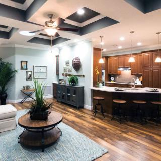 A modern open-plan living space featuring a stylish kitchen with wooden cabinets and bar stools, adjacent to a cozy living area with contemporary decor.