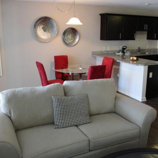 A modern living room with a sofa and cushion, adjacent to a kitchen area featuring red dining chairs.