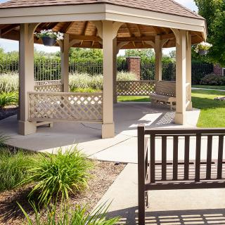 A serene park scene featuring a wooden gazebo surrounded by benches and lush greenery.