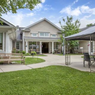 A well-maintained garden area with benches and a canopy in front of a residential building.