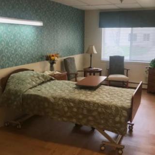 A well-furnished hospital room with a bed, chairs, and a window providing natural light.