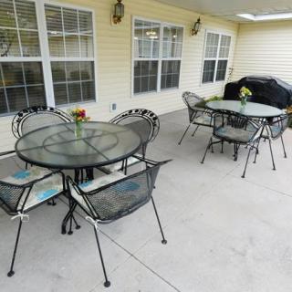 A cozy patio area with outdoor tables, chairs, a grill, and decorative flowers.