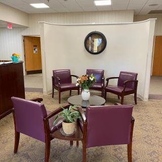 A cozy waiting area with purple chairs and a small table adorned with plants.