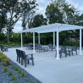 An outdoor seating area with a white pergola and patio furniture, surrounded by trees and landscaping.