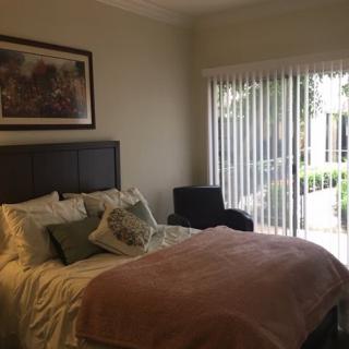 A cozy bedroom featuring a bed with pillows and a blanket, a large window with vertical blinds, and artwork on the wall.