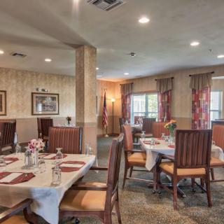 A cozy dining room with elegantly set tables and comfortable chairs, featuring warm decor and soft lighting.