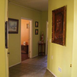 A cozy hallway with artwork adorning yellow walls, leading to another room.