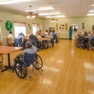 A community room in a nursing home with several seniors seated in wheelchairs.