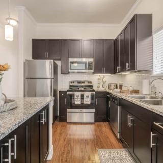 A modern kitchen with dark cabinets, stainless steel appliances, and granite countertops.