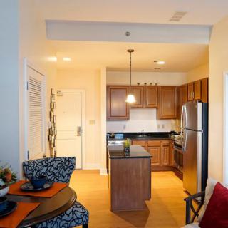 A modern apartment kitchen with an adjacent dining area, featuring wooden cabinets and stainless steel appliances.