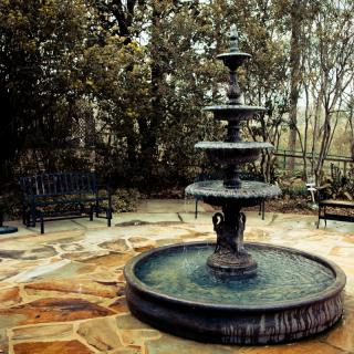 A multi-tiered fountain in a serene garden setting, surrounded by nature.