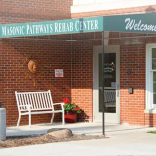 Entrance to a building with a green awning labeled 'Masonic Pathways Rehab Center' and a white bench.