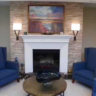 A cozy living room with a central fireplace, framed by two blue armchairs, and adorned with artwork above the mantel.