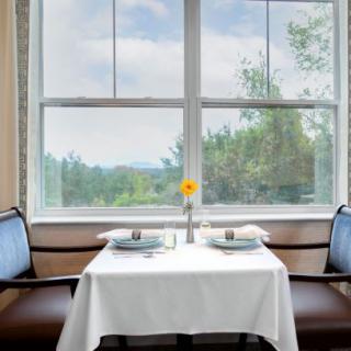 A cozy dining setup for two with a sunflower centerpiece, offering a scenic window view.
