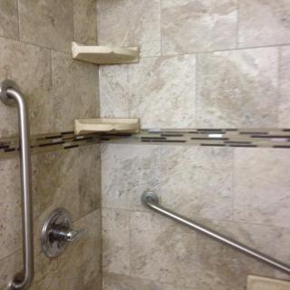 A bathroom shower with tiled walls, equipped with grab bars and soap holders.