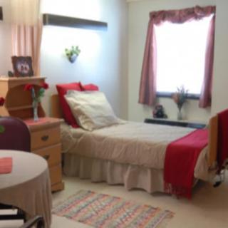 A cozy bedroom with a neatly made single bed adorned with red accents and a window with matching curtains.