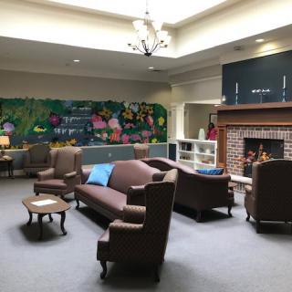 A cozy lounge area with sofas, armchairs, and a fireplace, featuring a colorful mural on the wall.