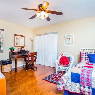 A cozy bedroom featuring a bed with a colorful quilt, a wooden desk, and a ceiling fan.