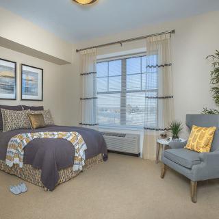 A cozy bedroom with neutral decor, featuring a comfortable bed and a stylish chair by the window.