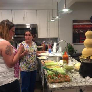 Two people having a conversation in the kitchen with a chocolate fountain and food on the counter.