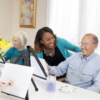 A caregiver assisting elderly individuals in a painting class.